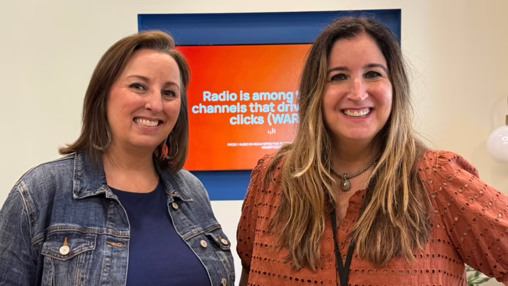 two smiling women next to a screen about radio s role in driving clicks.jpg